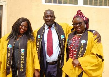 Three students from Nasarawa State University, dressed in bright yellows gowns, stand together smiling at the camera